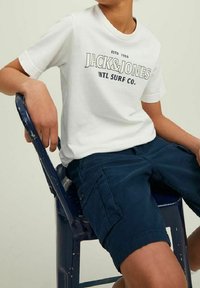 T-Shirt bianco in cotone con grafica "JACK & JONES INTL SURF CO." in nero, abbinato a pantaloni cargo blu navy con tasche laterali.