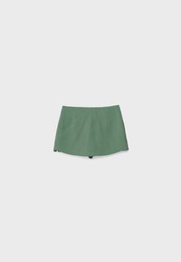 Mini-jupe verte trapèze avec des détails de coutures subtils, posée à plat sur un fond gris clair uni.