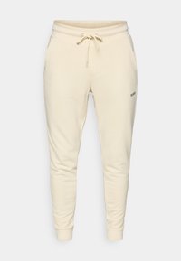Cream-colored sweatpants made of soft fabric, featuring an elastic waistband with drawstring, side pockets, and ribbed cuffs.