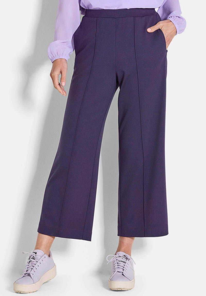 Marineblauwe wijde pantalon met details van een voornaad, een elastische tailleband en zijzakken, gecombineerd met lichtpaarse schoenen.