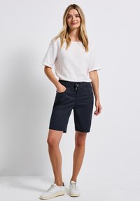 Shorts navy avec une taille élastique et un cordon de serrage, associés à un haut en lin blanc ample et des baskets blanches.