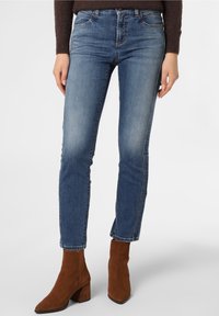 Blå denimjeans med mellan hög midja, slim fit och blekningsdetaljer, i kombination med bruna mocka ankelstövlar och en mörk tröja.