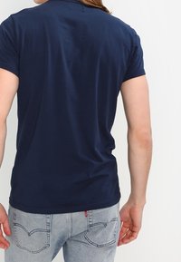 Granatowa koszulka polo z krótkim rękawem, wykonana z miękkiej bawełny. Posiada gładką fakturę i lekko zaokrąglony dół.