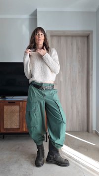 Overdimensjonert beige strikkegenser, grønne vide cargobukser med sidelommer, svart belte med sølvnagle, og svarte ankelstøvler.