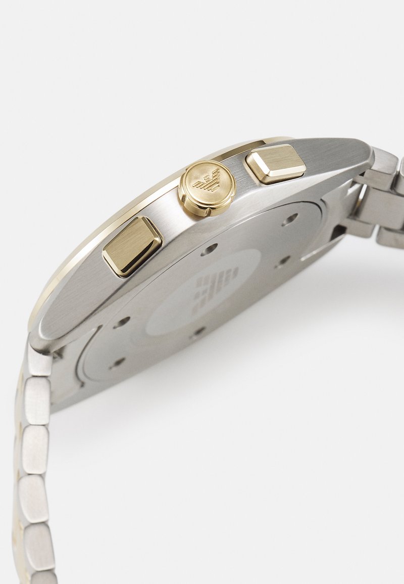 Silberner Edelstahlchronograph mit einem goldenen Akzent auf der Krone und den Drückern; verfügt über eine gebürstete Oberfläche und ein strukturiertes Armband.