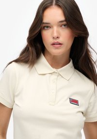 Crème polo shirt van katoen met een gestructureerde afwerking. Heeft een kraag, korte mouwen en een genaaid label op de linkerborst.