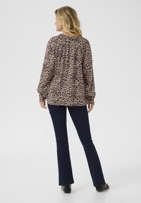 Blouse à imprimé léopard en beige et brun, avec des manches longues et un encolure ronde. Associée à un jean évasé bleu foncé et à des chaussures noires.