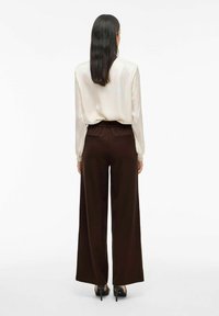 Pantaloni larghi marroni con una vestibilità rilassata, vita elasticizzata e due tasche posteriori, abbinati a una blusa in satin beige.
