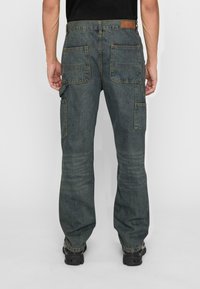 Denim cargo pants in dark blue with multiple pockets, visible stitching, straight-leg cut, and a leather patch at the back waist.