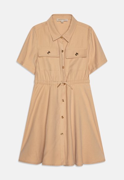Skjortekjole i lys beige stoff med korte ermer, to brystlommer, gullknappe-detaljer og snøring i livet for justerbar passform.