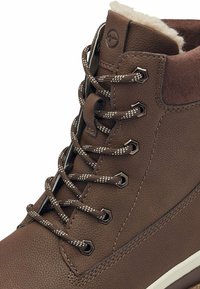 Bruine leren enkelboot met textuurmaterialen, een gewatteerde kraag, metalen oogjes en contrasterende veters met reflecterende draden.