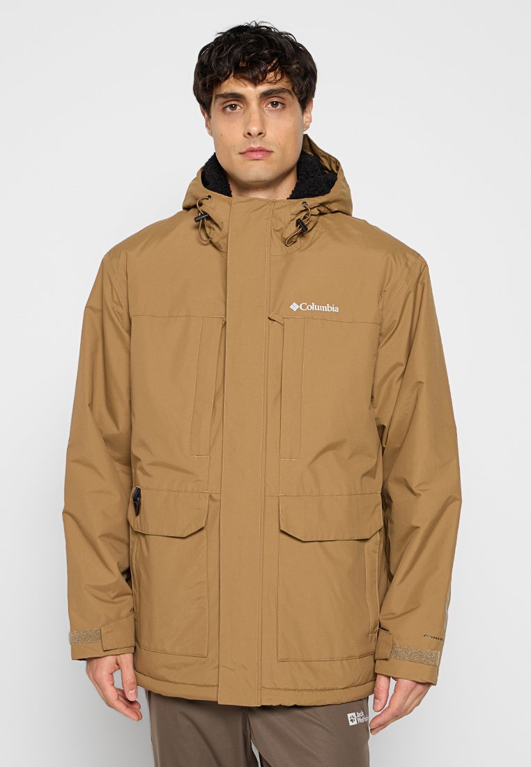 Veste imperméable marron avec une capuche, comprenant deux poches avant, des poignets élastiques et un intérieur en polaire. Logo de la marque sur la poitrine.