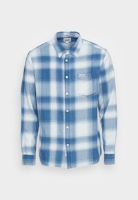 Chemise à carreaux bleue en coton tissé. Elle présente un col boutonné, des manches longues, une poche poitrine et des boutons blancs.