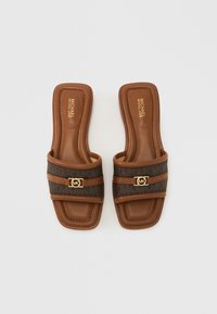 Brune slip-in sandaler med en struktureret brun overdel med logo-accent, flad sål og firkantet tådesign.