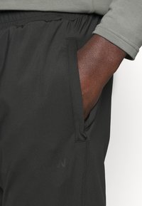 Svarta sportbyxor med elastisk midja, med sidofickor och ett mjukt, strukturerat tyg. Diskret logotypdetalj nära fickan.