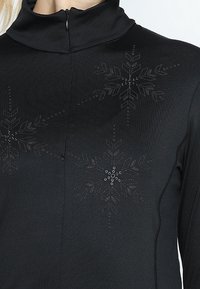 Pullover nero con colletto alto e chiusura con zip, caratterizzato da motivi a fiocco di neve con texture e un leggero luccichio, accentuato da un design aderente e cuciture laterali.