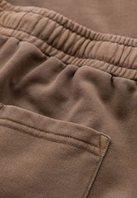 Jogging en coton marron avec une taille élastique et une poche latérale, présentant des détails de coutures visibles et une texture douce.
