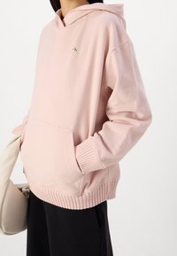 Felpa con cappuccio rosa chiaro realizzata in tessuto morbido, con polsini e orlo a coste, tasca a marsupio anteriore e una piccola toppa con logo.
