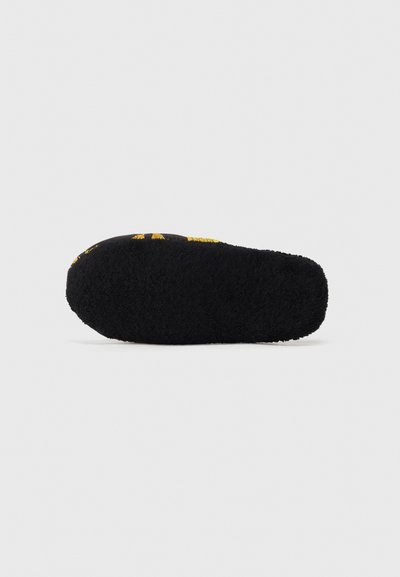 Svart toffel med en texturerad, fluffig botten. Ovandelen har gula tryckta designelement. Rundad form med en mjuk, plyschig yta.