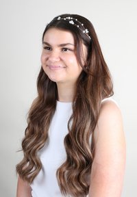 Accessorio per capelli a forma di corona con perline trasparenti e filo, caratterizzato da un disegno delicato, simile a fiori. Indossato da una persona con capelli lunghi e mossi.