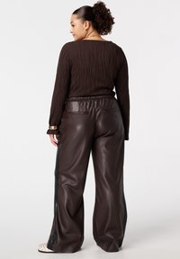 Haut marron à manches longues côtelé avec une texture ondulée, associé à un pantalon large en cuir synthétique marron avec des accents latéraux et des poches arrière.