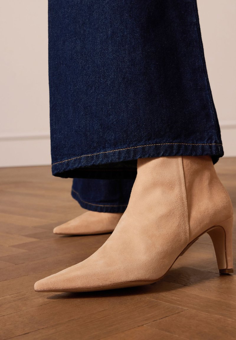 Bottines en daim beige avec un bout pointu et un talon de 5 cm, associées à un pantalon en denim noir à larges jambes avec un ourlet effiloché.