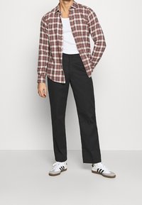 Rød og hvid rute langærmet skjorte, sorte bukser og hvide sneakers med sorte striber; afslappet pasform med en simpel crew neck undertrøje.