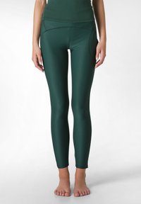 Leggings verde scuro realizzati in un materiale liscio e stretch. Presentano una vita alta e tasche laterali, con un design elegante e aderente.