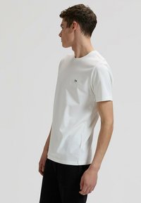 Λευκό βαμβακερό T-shirt με στρογγυλή λαιμόκοψη, κοντά μανίκια και μικρό μαύρο λογότυπο "Lee" στο στήθος. Απλός, ευθύς σχεδιασμός.