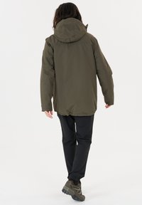 Olivgrön utomhusjacka med huva, utformad för komfort. Har en lös passform och bärs med svarta byxor samt praktiska skor.