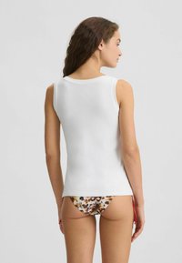 Top alb fără mâneci, cu decolteu rotund, formă ajustată și textură netedă. Asortat cu costum de baie cu un model floral.