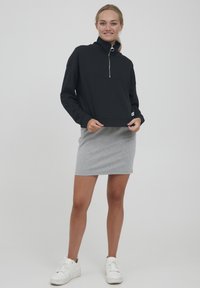 Black zip-up sweatshirt with high collar and front pocket, paired with a light gray knee-length skirt, worn with white sneakers.