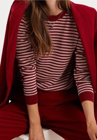 Röd randig tröja i mjukt stickat material med vita horisontella linjer. Ribbad mudd och krage. Bärs under en matchande röd blazer.