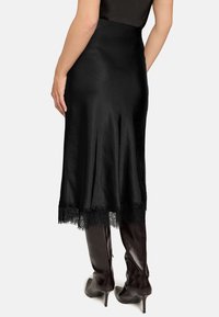 Schwarzer Satinstrock mit einem Spitzenbesatz am Saum, von hinten gezeigt, kombiniert mit braunen High-Heel-Stiefeln. Glatte Textur und figurbetontes Design.