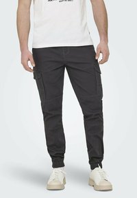 Czarne spodnie cargo z kieszeniami bocznymi, tapered fit, elastycznymi mankietami i kontrastowym przeszyciem. W połączeniu z białymi sneakersami i t-shirtem.