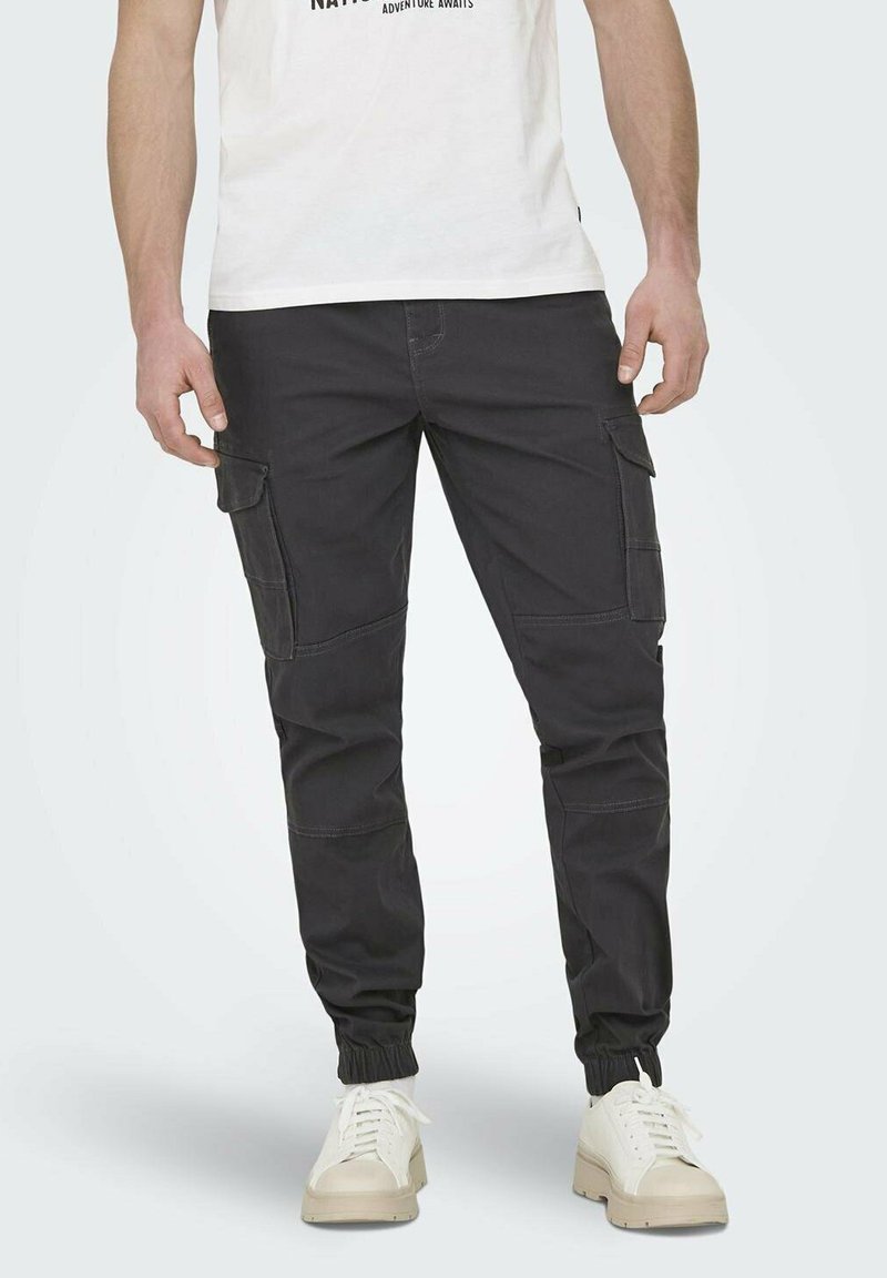 Czarne spodnie cargo z kieszeniami bocznymi, tapered fit, elastycznymi mankietami i kontrastowym przeszyciem. W połączeniu z białymi sneakersami i t-shirtem.