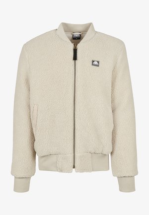 Kreemivärvi bomber jope, mis on valmistatud tekstureeritud fliisist, esiosa tõmbluku, ribatud ääride ja rinnal oleva embleemiga.