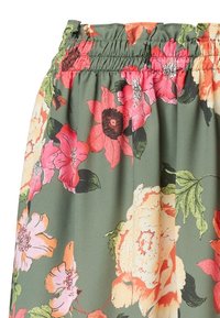 Floral skirt met een geplooid tailleband, met grote roze en oranje bloemen op een groene achtergrond. Soepele stof, net boven de knie.