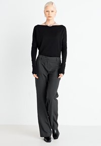 Black long-sleeve shirt with a boat neckline, paired with dark gray tailored trousers. The pants feature a loose fit and are complemented by black heels.