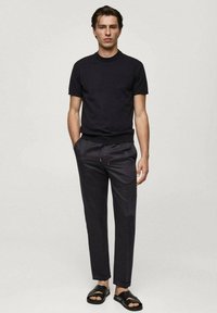 Black short-sleeve t-shirt, slim-fit, paired with dark tapered trousers and black slide sandals. Minimalist design and soft texture.