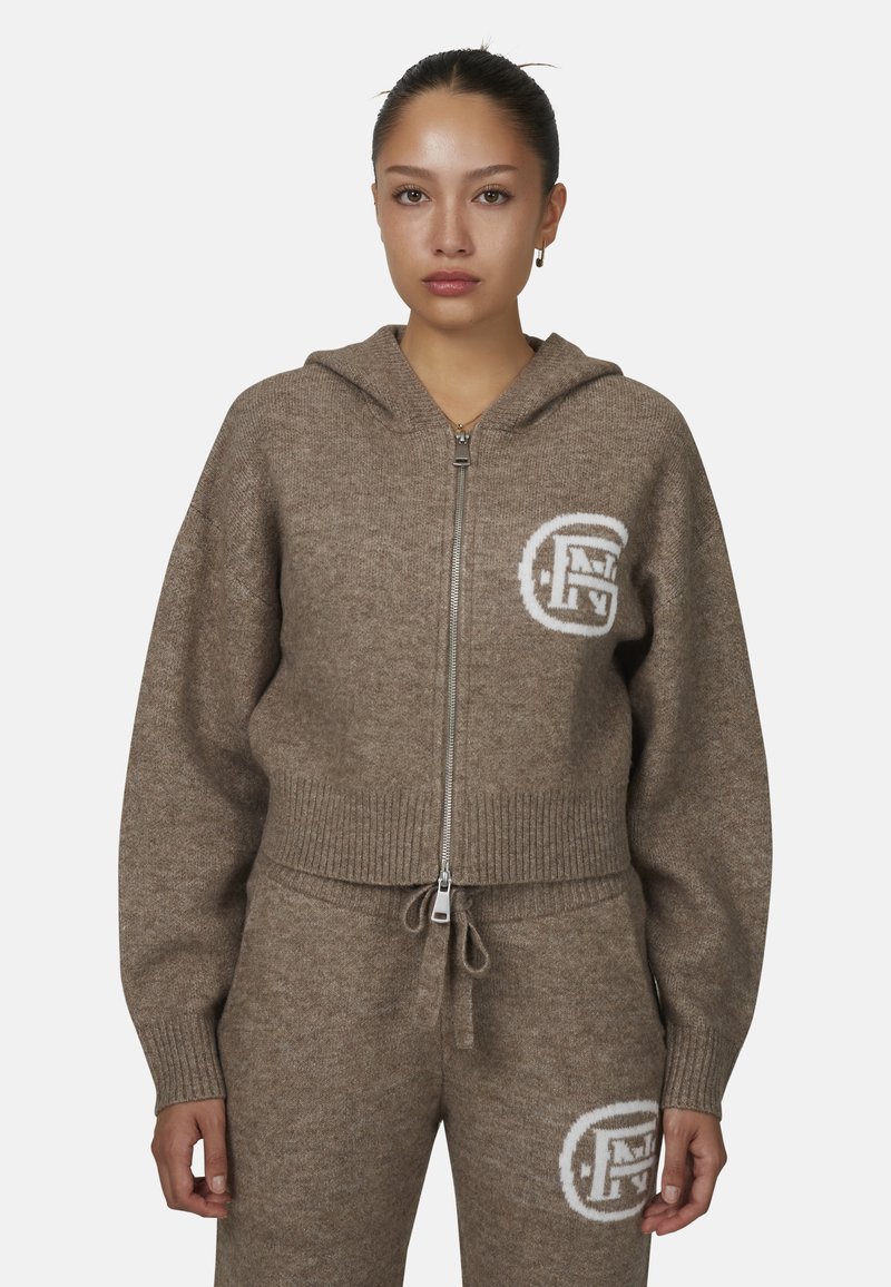 Brązowa bluza z zamkiem wykonana z miękkiego materiału, z prążkowanym dołem, dużym kapturem i białym logo po lewej stronie klatki piersiowej.