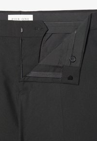 Schwarze Hose mit Reißverschluss, Knopfdetails und glatter Textur. Das Innere zeigt einen gefütterten Bund und Nähte als Akzent.