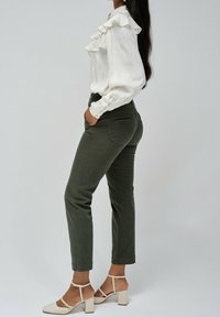 Bílá rýškovaná blůza s dlouhými rukávy, spárovaná s olivovými slim kalhotami a béžovými sandály na blokovém podpatku. Vyznačuje se hladkým textilním povrchem.