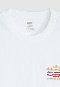 Witte katoenen t-shirt met een ronde halslijn. Heeft meerkleurige geborduurde tekst: "Een Amerikaanse Legende", "Levi Strauss" en "Een Traditie Sinds."