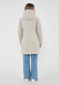 Parka isolata beige chiaro con cappuccio, caratterizzata da una texture liscia e tasche laterali, abbinata a jeans in denim a vita alta e sneakers bianche.