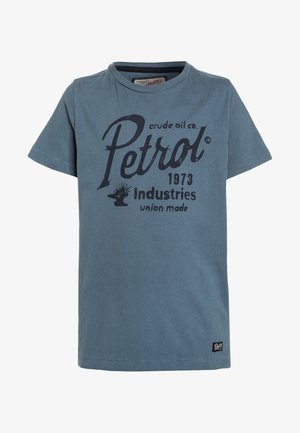 T-shirt bleu à manches courtes avec texte foncé "Petrol crude oil co. 1973 industries union made" et une petite étiquette noire près de l'ourlet.