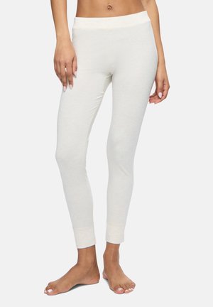 Mujer con leggings ajustados color marfil con cinturilla elástica, de pie descalza sobre un fondo claro y liso.
