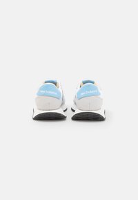 Bílé a světle modré tenisky New Balance s šedými akcenty, vybavené odolnou podrážkou, hladkým textilním svrškem a výrazným logem značky na patě.
