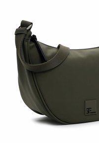 Borsa a spalla verde oliva realizzata in materiale morbido e strutturato, caratterizzata da una forma curva, tracolla regolabile e dettaglio con logo in rilievo.