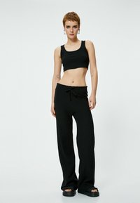 Top corto nero e pantaloni neri larghi con elastico in vita, dotati di cordoncino. Texture liscia e design minimale.